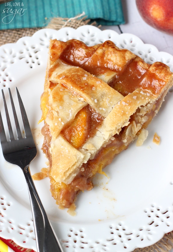A close up of a slice of Peach Pie next to a fork on a white plate