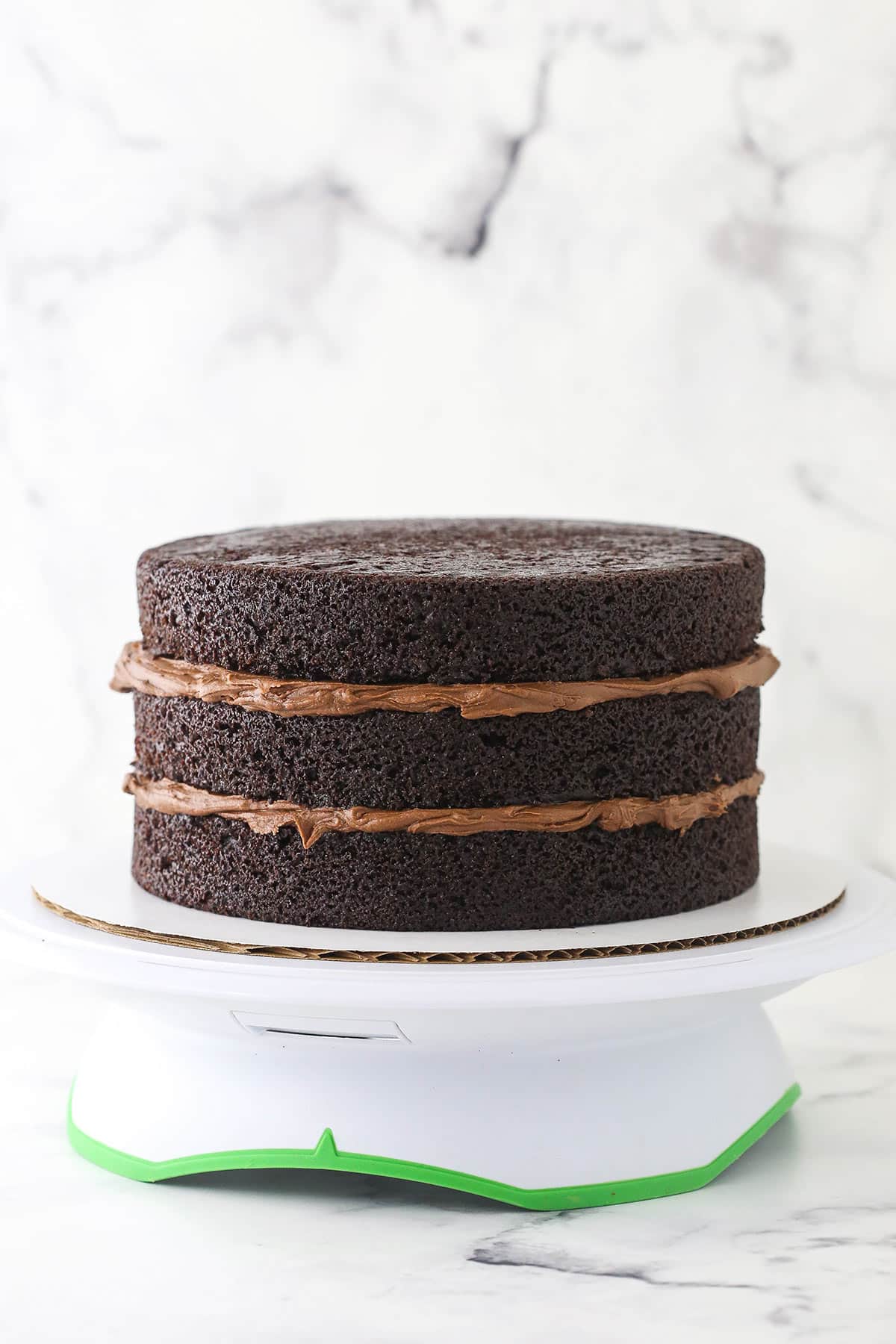 3 layers of chocolate cake on a cake stand with frosting in between each layer