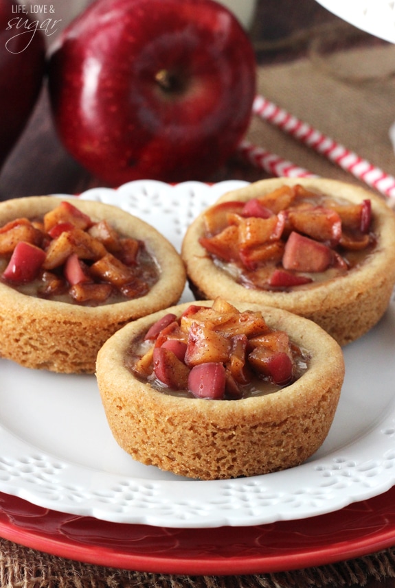 A close-up shot of three caramel apple cookie cups with a fresh red delicious apple behind them