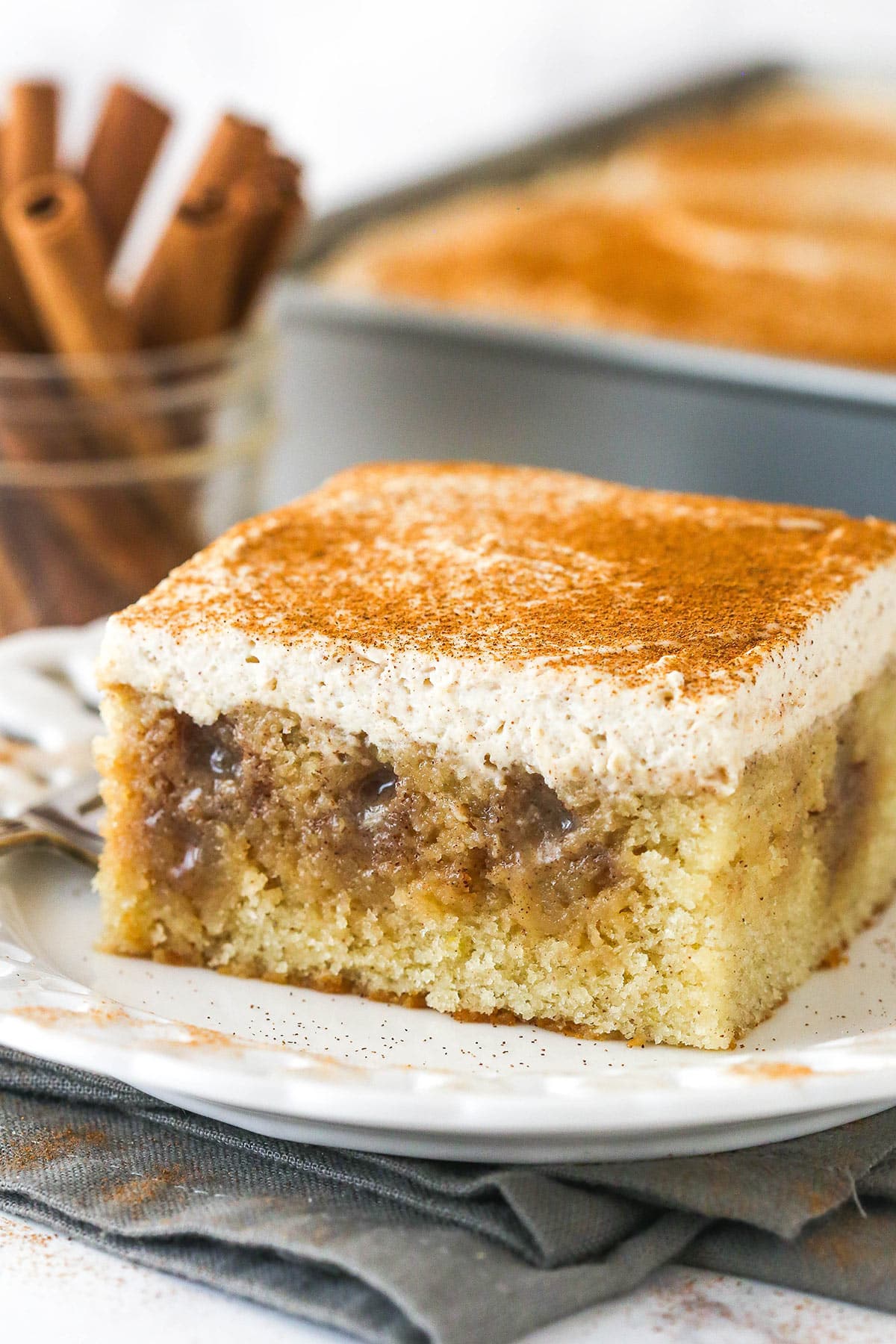 This Cinnamon Roll Poke Cake is perfectly spiced, ultra moist, and easy to make, with a cinnamon sugar sauce and whipped frosting. A slice of cinnamon roll poke cake on a plate