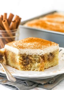 A slice of cinnamon roll poke cake on a plate with a bite missing
