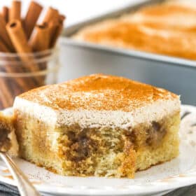 A slice of cinnamon roll poke cake on a plate with a bite missing