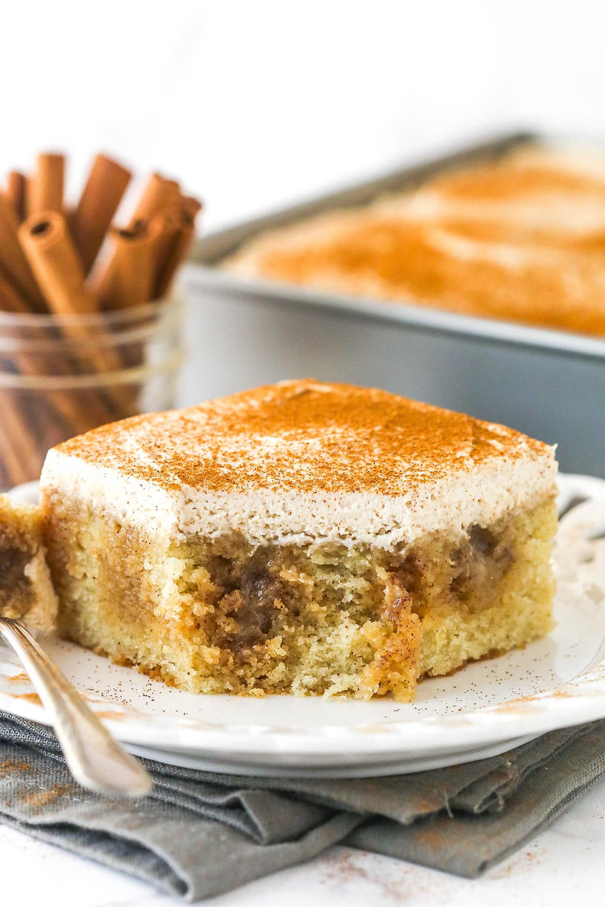 A slice of cinnamon roll poke cake on a plate with a bite missing