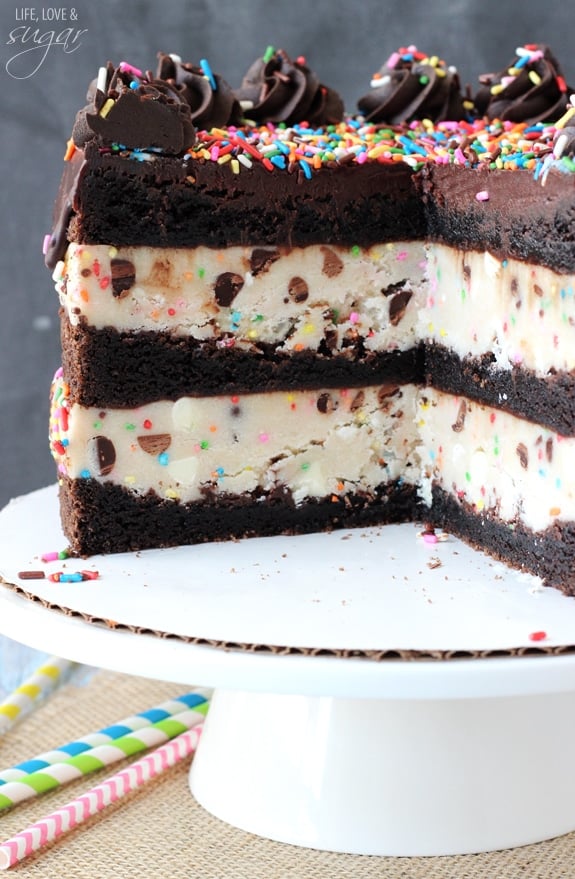 Funfetti Cake Batter Cookie Dough Brownie Layer Cake on a white cake stand with a couple slices removed