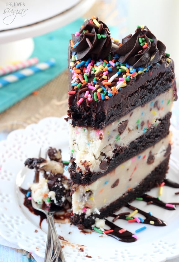 A slice of Funfetti Cake Batter Cookie Dough Brownie Layer Cake on a white plate with a bite on a fork