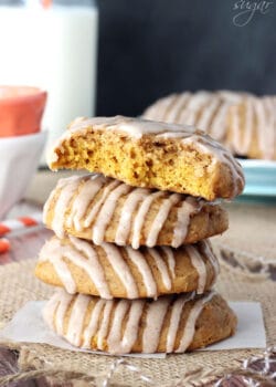 A stack of four pumpkin spice cookies on a small piece of wax paper with the top one missing two big bites