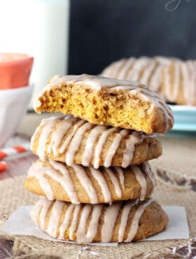 A stack of four pumpkin spice cookies on a small piece of wax paper with the top one missing two big bites