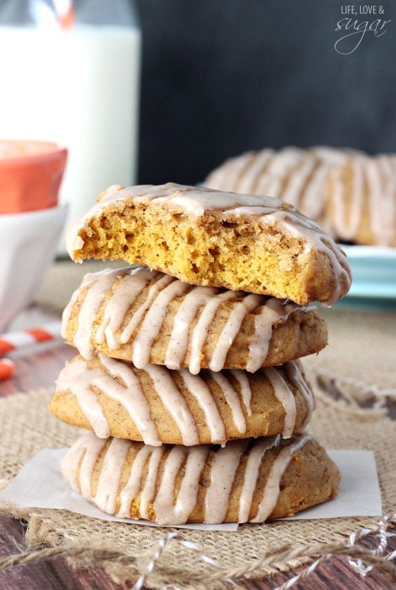 These moist and tender pumpkin cookies are full of fall spice and everything nice! They're drizzled with a smooth cinnamon glaze and absolutely packed with pumpkin. A stack of four pumpkin spice cookies on a small piece of wax paper with the top one missing two big bites.