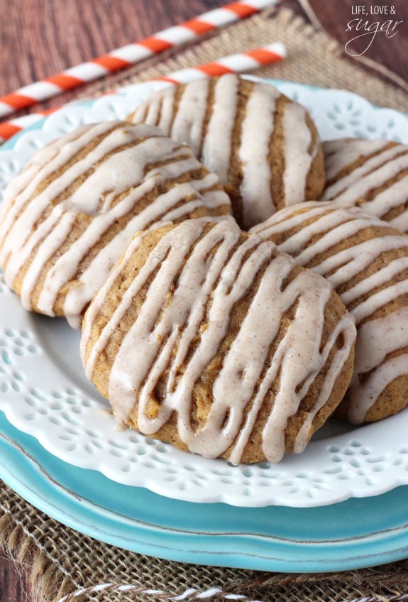 A plate of pumpkin cookies drizzled with cinnamon glaze featuring two orange and white striped straws in the background