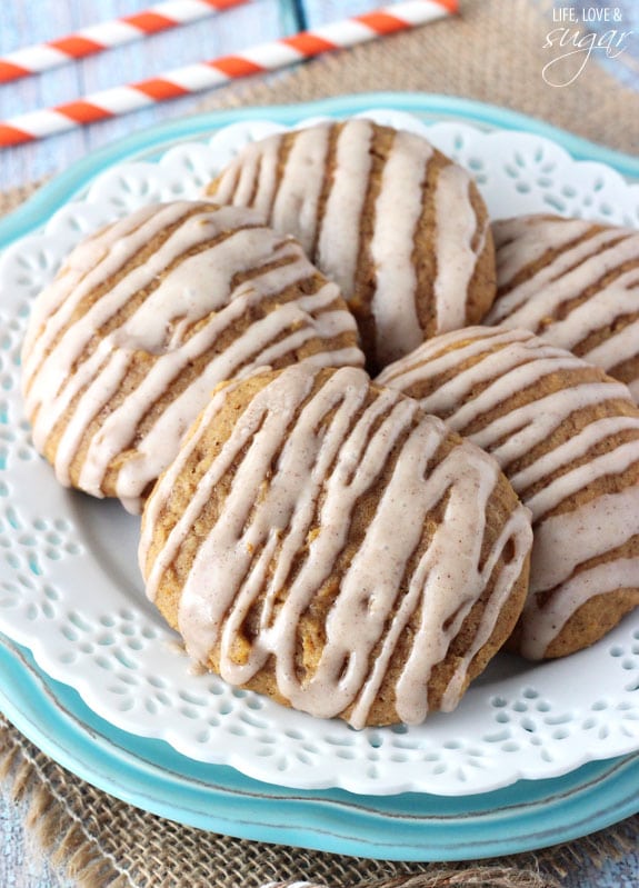 A plate of pumpkin cookies with cinnamon glaze on top and two straws in the background.