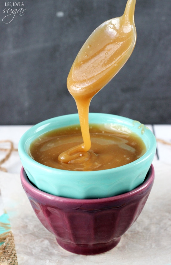A spoon drizzling caramel sauce into a green and purple stacked bowl set