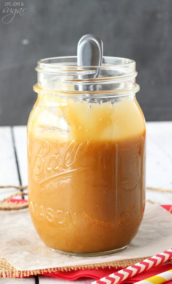 A jar full of brown sugar caramel sauce with a spoon sticking inside