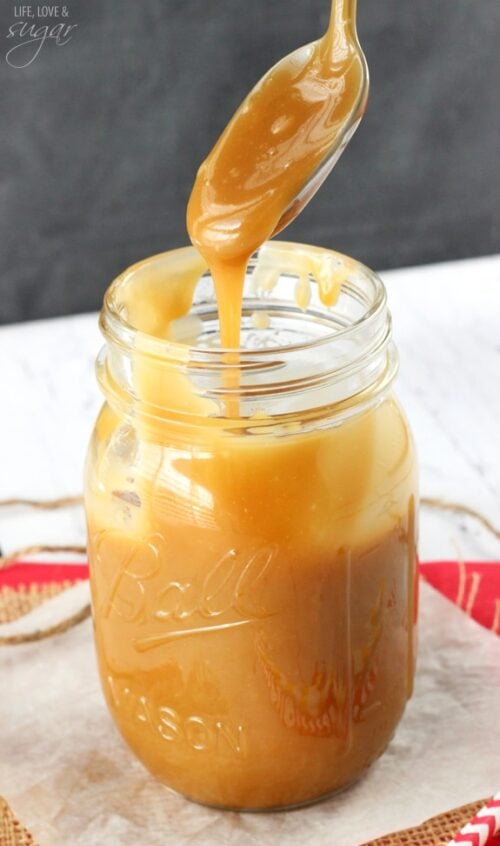 A spoon drizzling some caramel sauce back into the mason jar below it