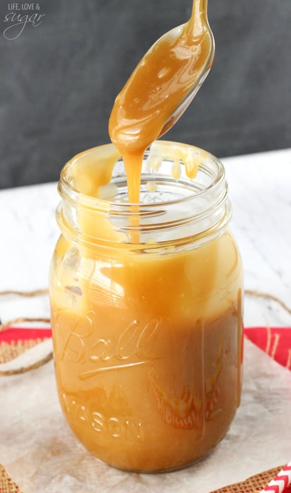 A spoon drizzling caramel sauce into a mason jar