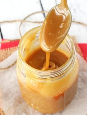 A spoonful of homemade brown sugar caramel sauce being drizzled down into a jar filled with more caramel