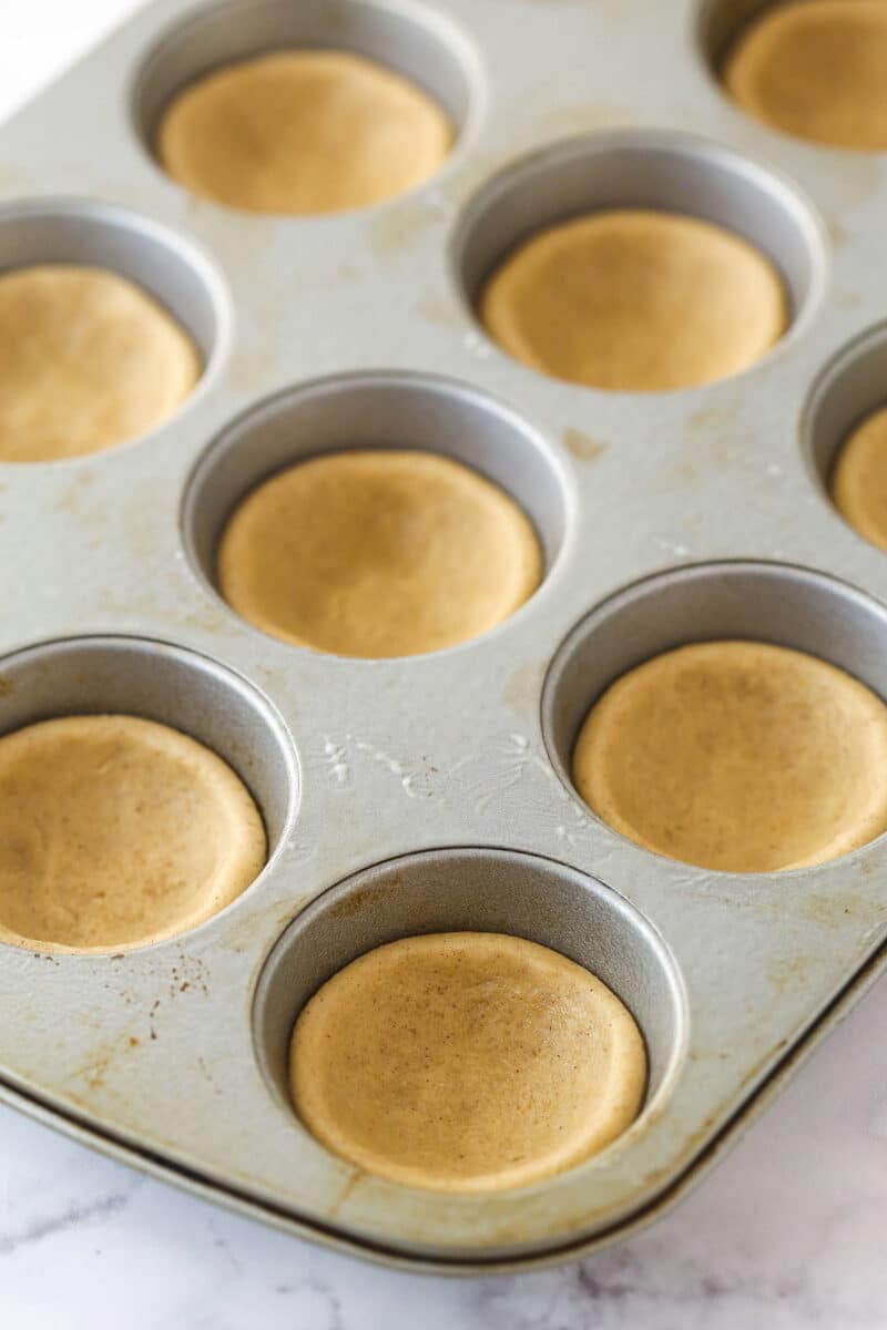 a cupcake pan with cookie dough pressed down into each cup