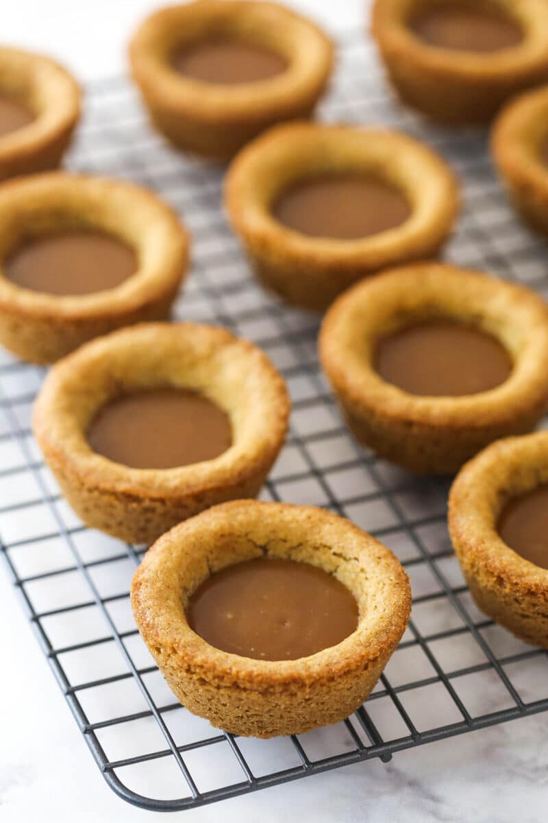 cookie cups on a cooling rack with caramel filled in the centers
