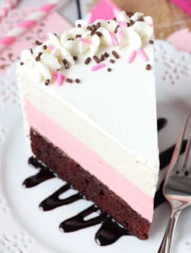 A piece of Neapolitan ice cream cake on a plate with a chocolate fudge drizzle