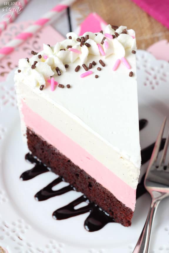 A piece of Neapolitan ice cream cake on a plate with a chocolate fudge drizzle