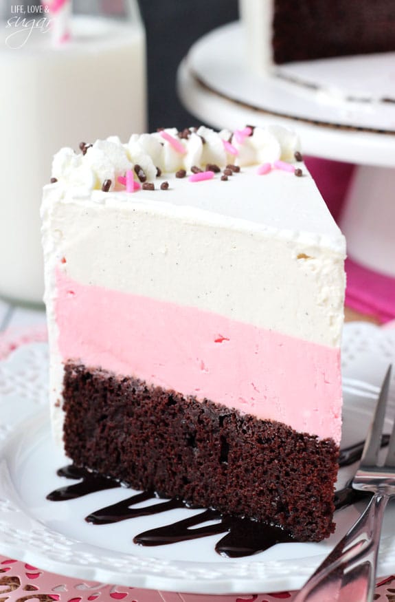 A big slice of Neapolitan ice cream cake on a dessert plate with a metal fork