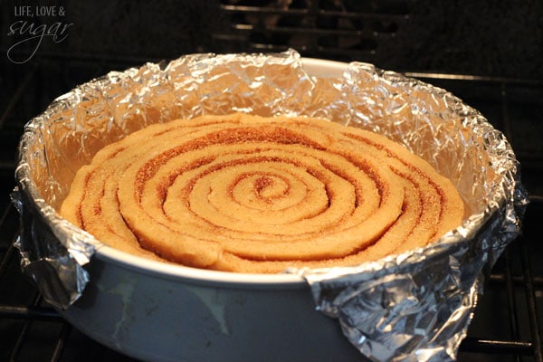 An Unbaked Cinnamon Roll Cookie Cake in a foil-lined pan in the oven