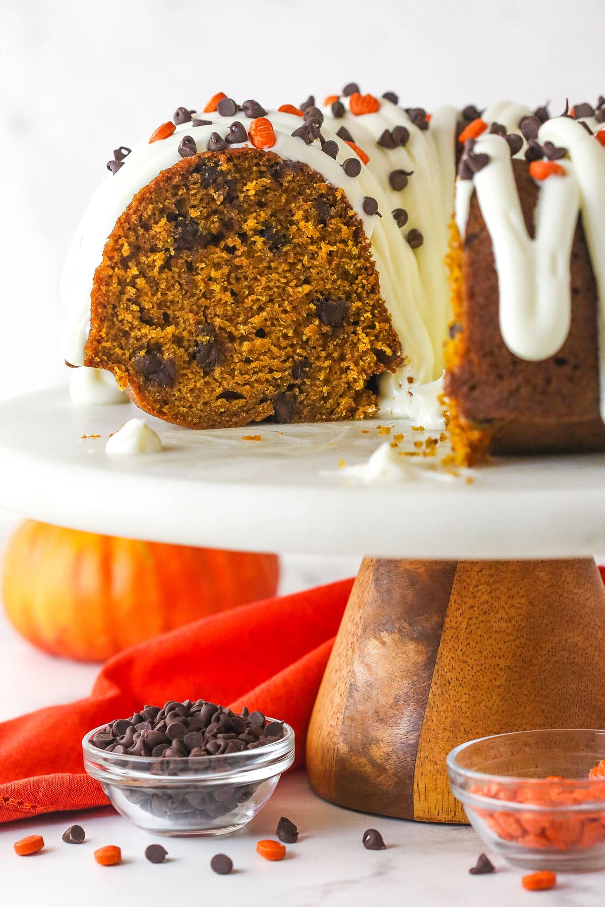 Every bite of this pumpkin chocolate chip bundt cake is moist, perfectly spiced, and dotted with chocolate chips. Pumpkin chocolate chip bundt cake on a cake stand with a slice missing