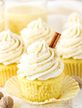 A Christmas eggnog cupcake with the liner removed and a cinnamon stick on top