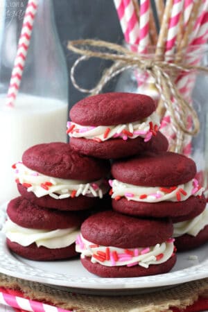 Red Velvet Cookie Sandwiches on white plate stacked with pink, red, white sprinkles