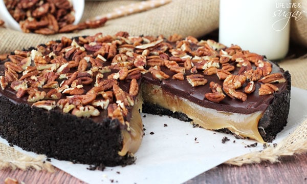 A gooey caramel turtle pie on a sheet of parchment paper with one large slice missing