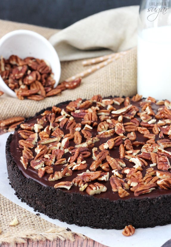A fully set caramel turtle pie on a sheet of parchment paper beside a spilled bowl of pecans