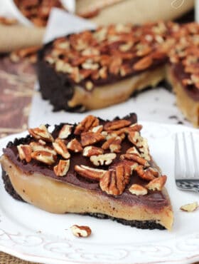 A piece of caramel turtle pie on a plate with the rest of the pie in the background