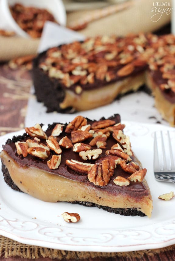 This easy no-bake Caramel Turtle Pie features a buttery chocolate crust, a gooey caramel filling, rich chocolate ganache and crunchy pecans! A piece of caramel turtle pie on a plate with the rest of the pie in the background