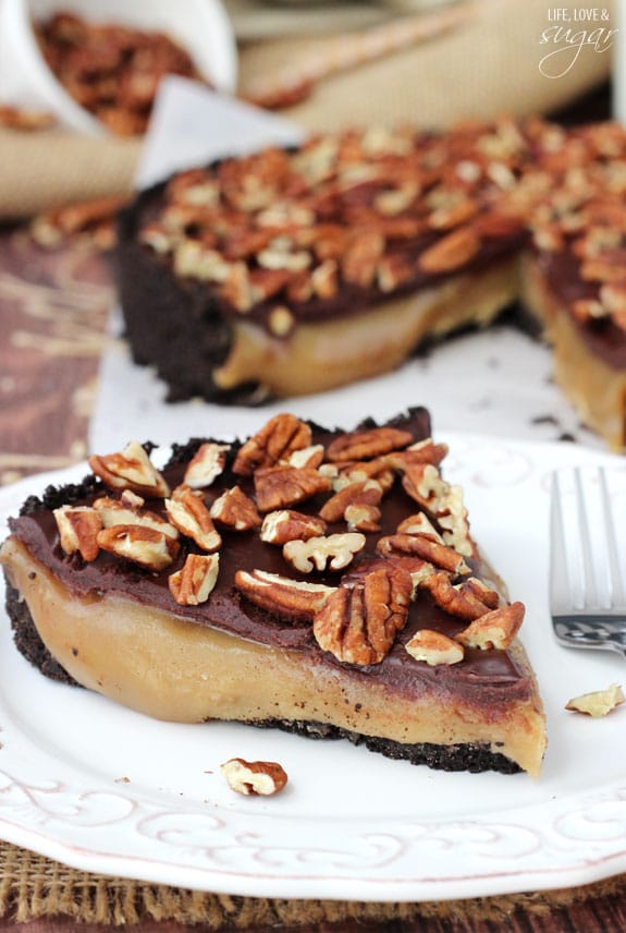 A piece of caramel turtle pie on a plate with the rest of the pie in the background