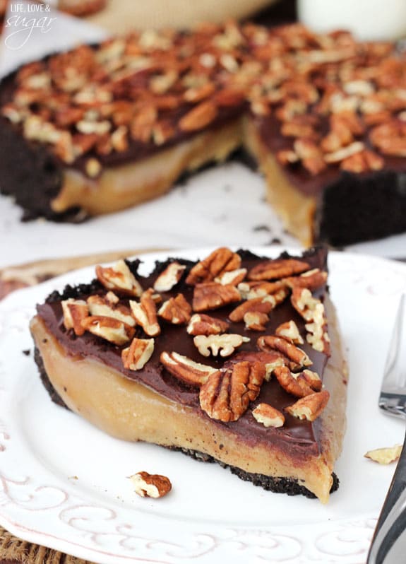 A slice of caramel chocolate pecan pie on a plate with the remaining pie behind it