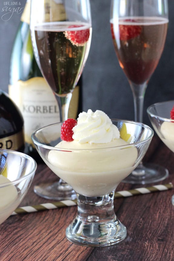 Mousse in a glass bowl with whipped cream and a raspberry on top with Black Raspberry Champagne Bellinis behind it