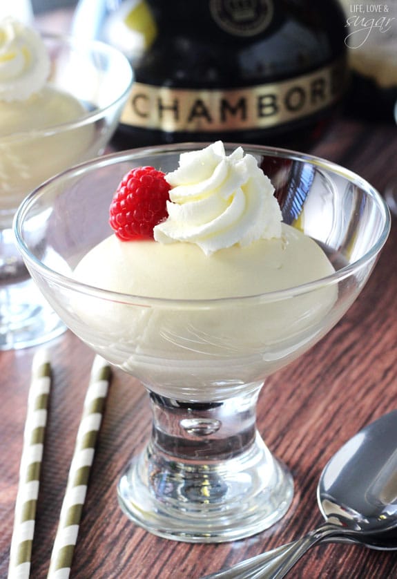 Fluffy mousse in a small glass bowl topped with a raspberry and whipped cream