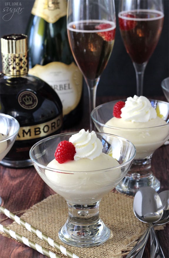 Two glasses with Mousse, whipped cream and a raspberries on top with Champagne Bellinis behind them