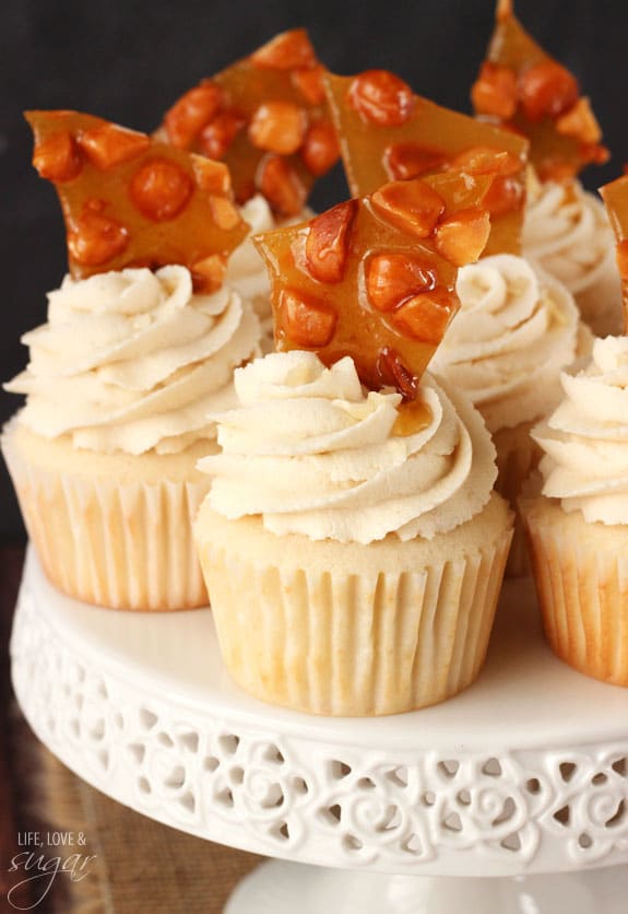 White cupcakes with icing and macadamia brittle on top of a white cake stand