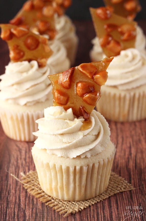 A white cupcake on a piece of burlap is topped with icing and macadamia brittle