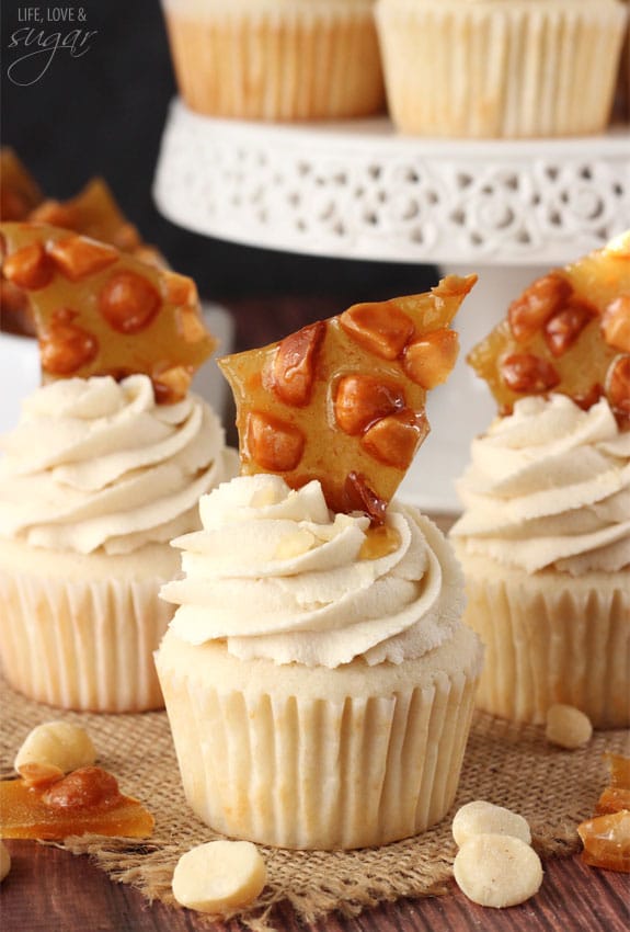 Three white cupcakes with icing and macadamia brittle on top