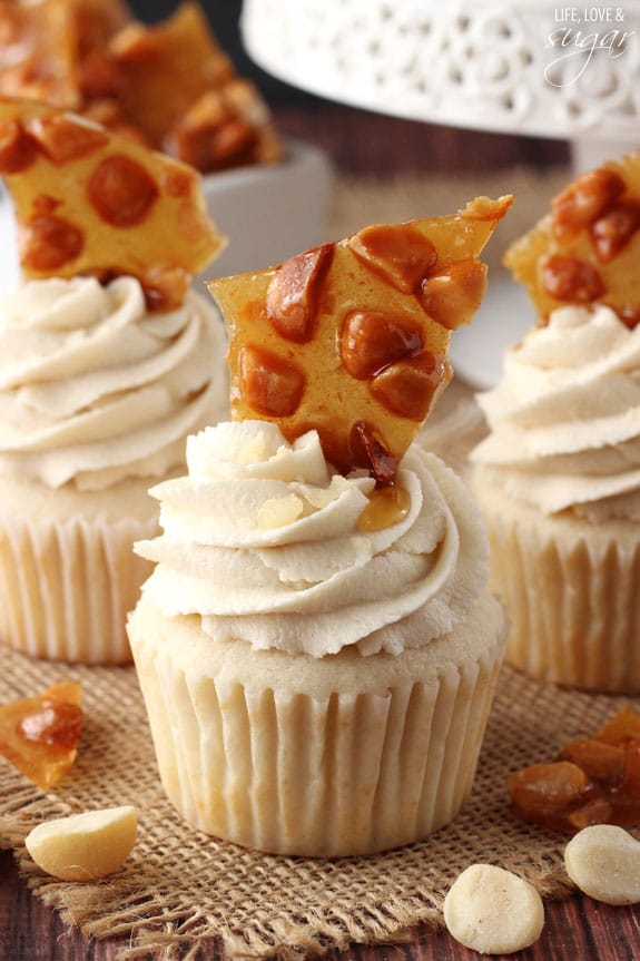 Close up of a Macadamia Brittle Cupcake surrounded by more cupcakes and nuts