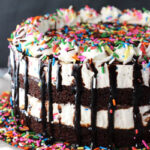 A brownie cake batter ice cream cake on a white cake stand on top of a dining table