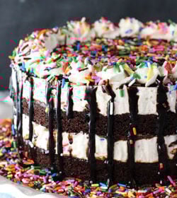A brownie cake batter ice cream cake on a white cake stand on top of a dining table