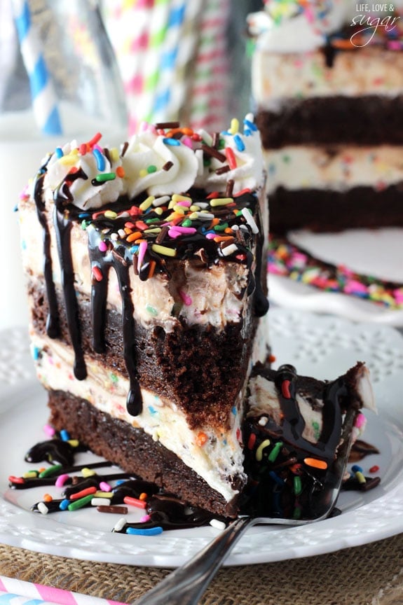 A piece of brownie ice cream cake on a plate with one bite on a fork