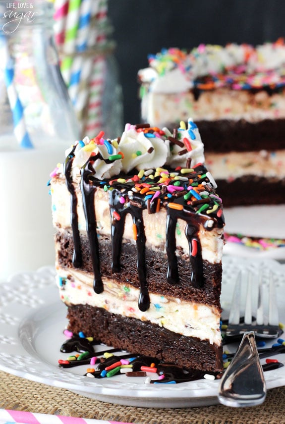 A slice of ice cream cake on a serving plate with the rest of the cake on a stand behind it