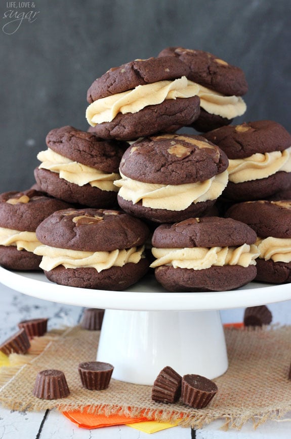 Peanut Butter Cookie Sandwiches stacked on white stand with Reese's cups around it