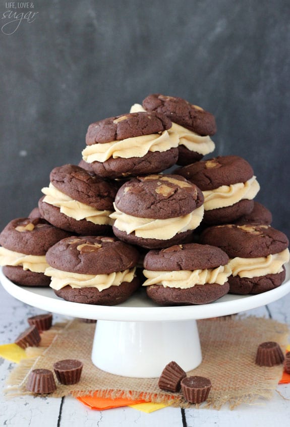 Peanut Butter Cookie Sandwiches stacked on white platter with Reese's candy around it