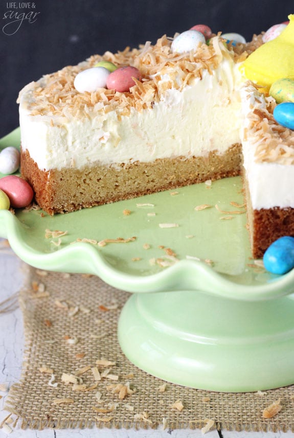 Coconut Blondie Cheesecake on a green cake stand with a slice removed