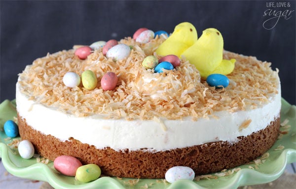 Coconut Blondie Cheesecake topped with Marshmallow Peeps and easter egg candies on a green cake stand