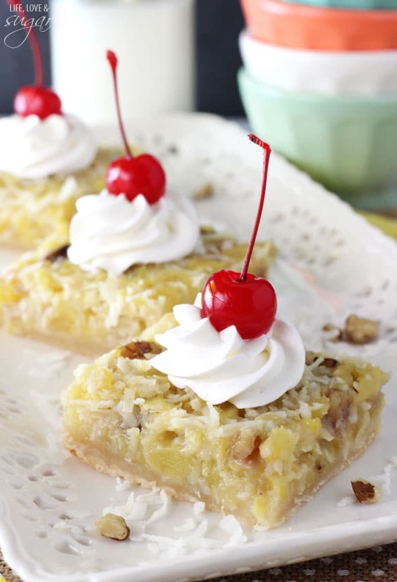 Pineapple Coconut Bars topped with whipped cream and a cherry on a platter